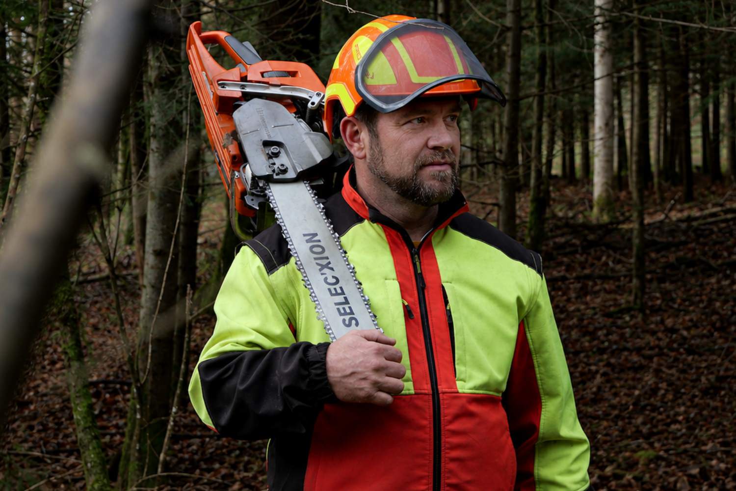 Professionnel forestier équipé d’un casque tenant une tronçonneuse en forêt